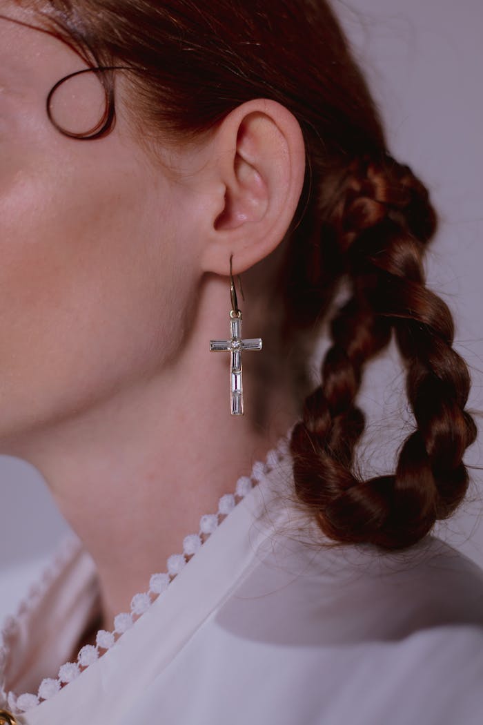 A close-up of a cross-shaped earring worn by a woman with braided hair.