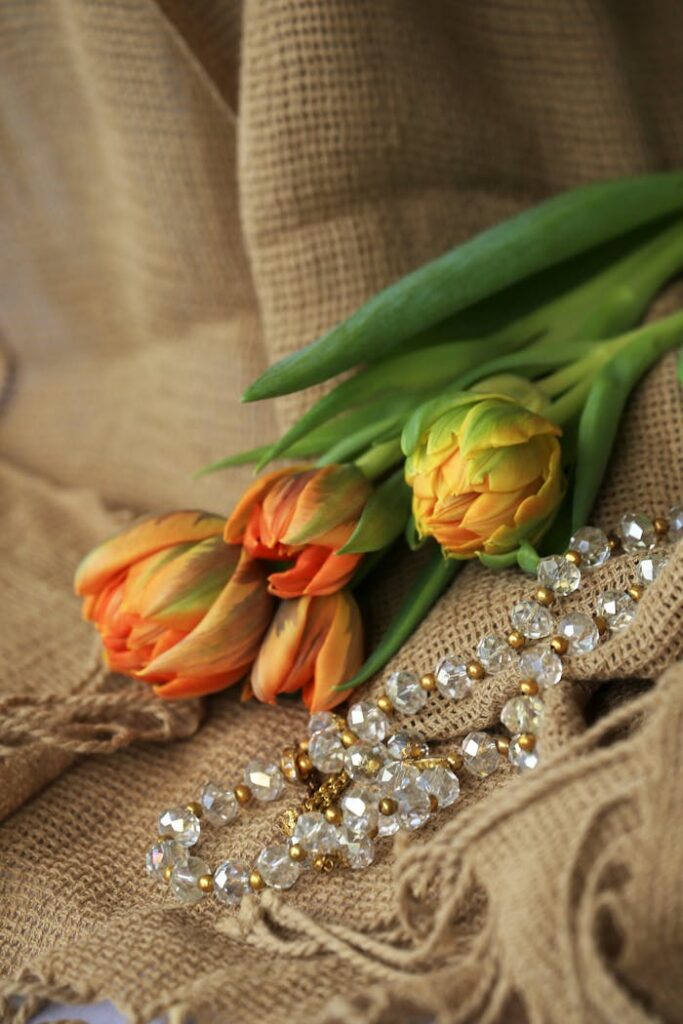 Orange tulips and crystal necklace on a burlap fabric background create an elegant, fresh composition.